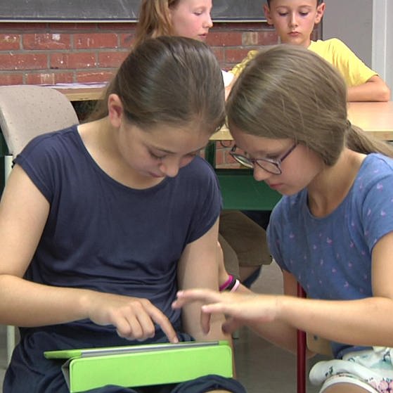 Zwei Mädchen sitzen in Klassenraum und nutzen gemeinsam ein Tablet