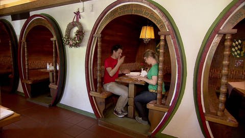 Zwei Personen sitzen in einem zu einer Sitzecke umgebauten Weinfass in einem Restaurant. 